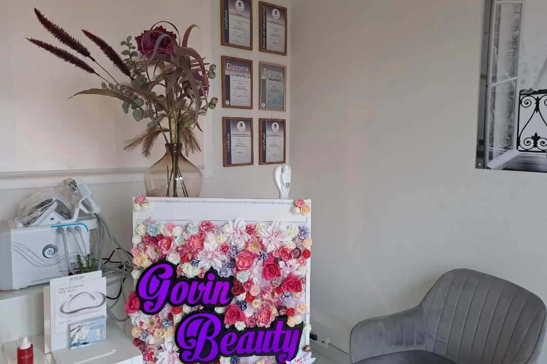Bloemenwand met het Govin Beauty logo en de diploma's van Nukhsha in de salon